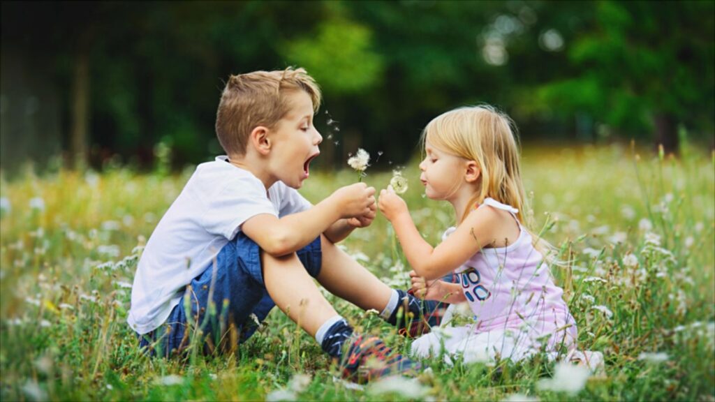 Zwei Kinder pusten Pusteblumen auf einer Sommerwiese